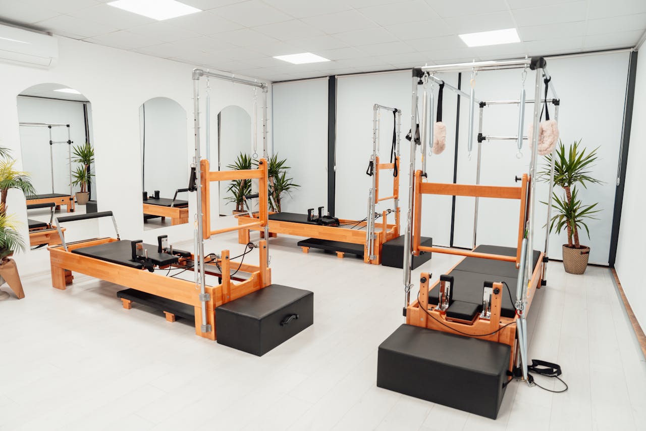 Bright, spacious Pilates studio featuring wooden pilates towers and lush plants.